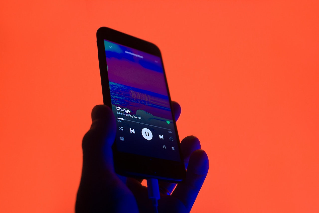 Person hält ein Smartphone mit einer geöffneten Musik-Streaming-App vor einem leuchtend roten Hintergrund