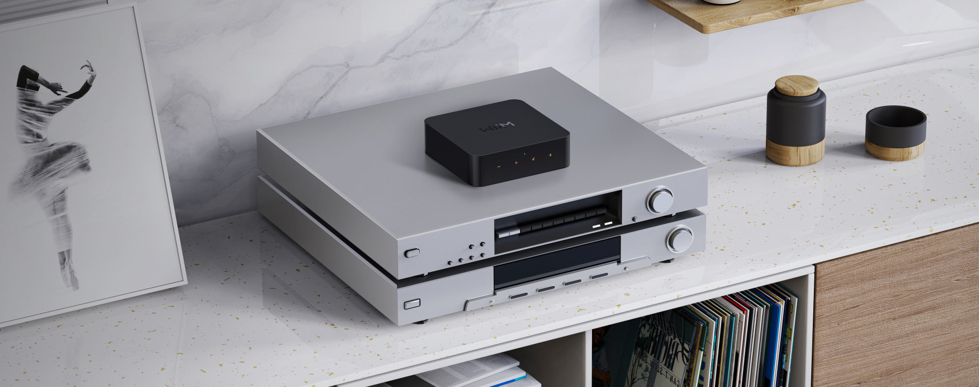 Das Bild zeigt einen grauen WiiM Pro Streaming-Adapter, der auf einem weißen Regal über einem CD-Player steht. Im Hintergrund sind ein gerahmtes Kunstwerk und zwei dekorative Gegenstände zu erkennen. Darunter befindet sich ein Regal mit Schallplatten.